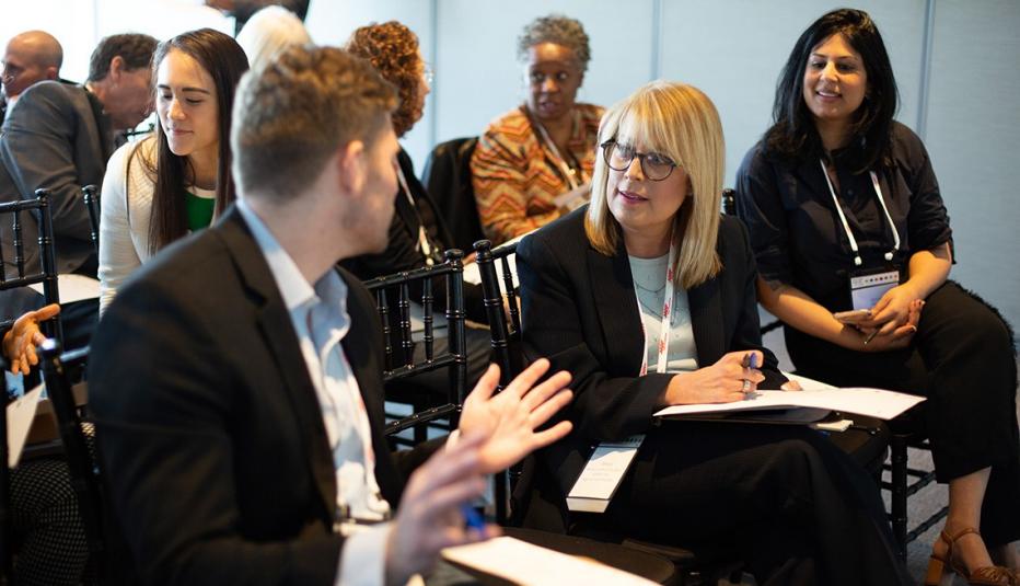 A man and a woman chatting in a conference room filled with attendees.