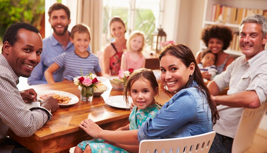 Family and friends sitting at a dining table, looking at camera