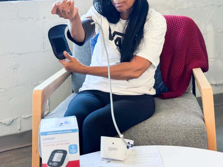 A woman places a blood pressure monitoring cuff around her upper right arm.
