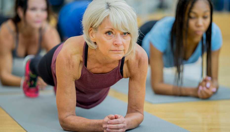 A group of adults are indoors at a fitness center. They are wearing casual exercise clothing. They are looking serious while doing plank exercises on yoga mats.
