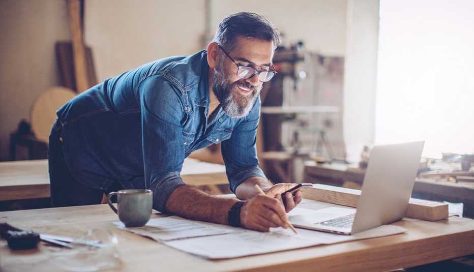 Carpenter in wood workshop using smart phone and working on project