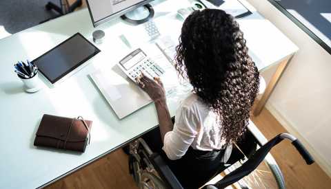 Middle aged disabled woman using a calculator at her desk