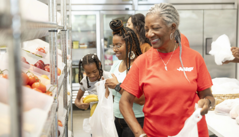 a woman in an a a r p volunteer shirt packing bags of food in a kitchen