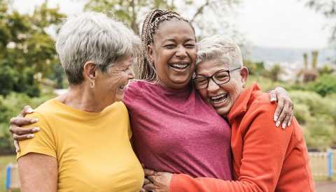 three women outdoors embracing each other and laughing