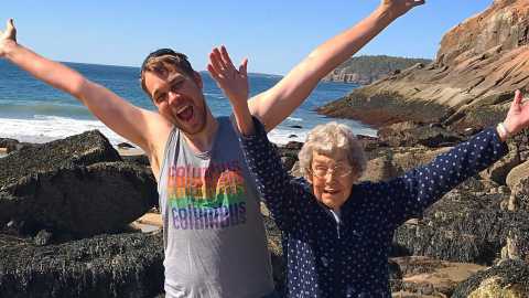 a man and woman smile and stretch out their arms in front of a coastal setting