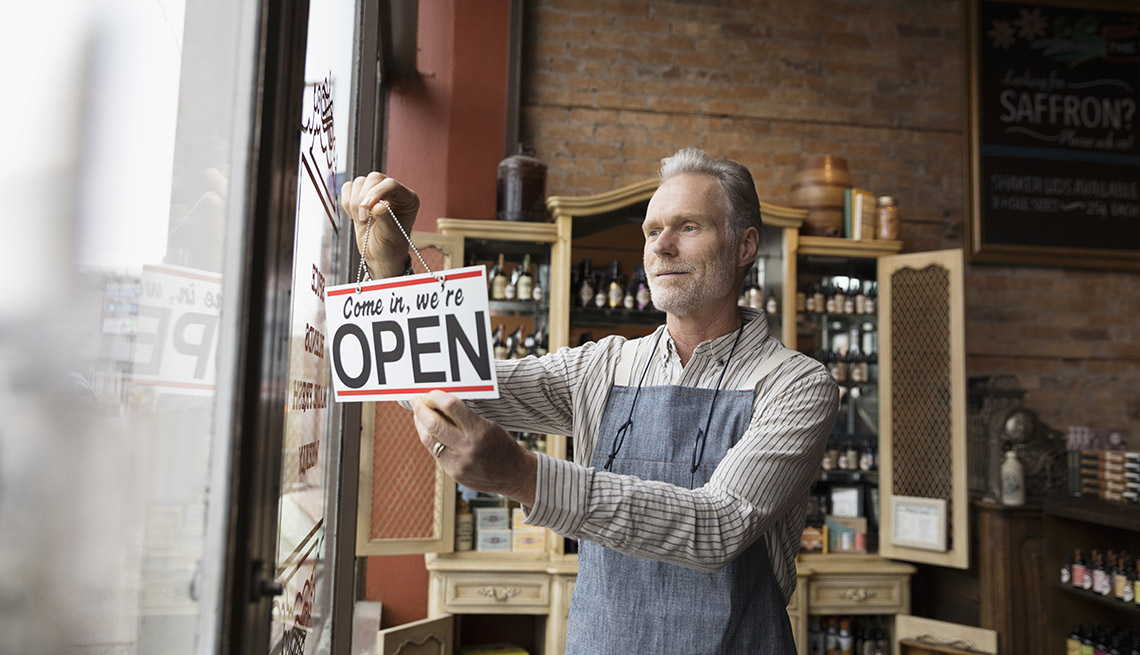 Male shop owner hanging open sign in spice shop window