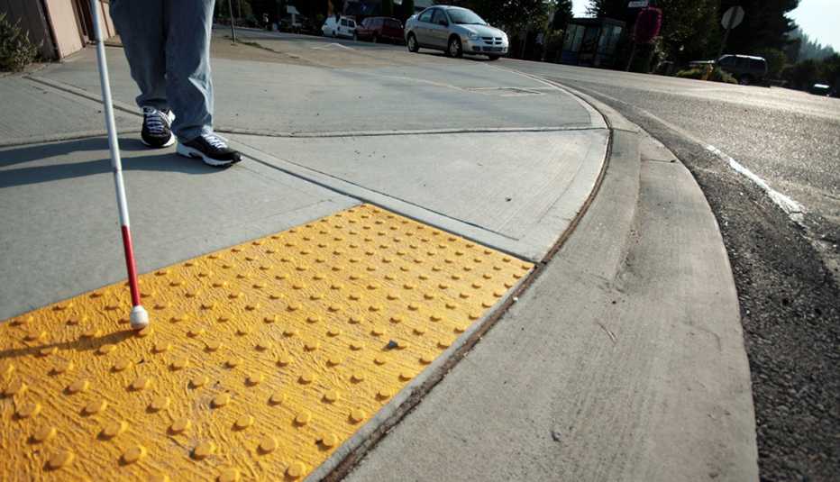 closeup of a persons feet and cane feeling their way on accessibility bumps on a sidewalk
