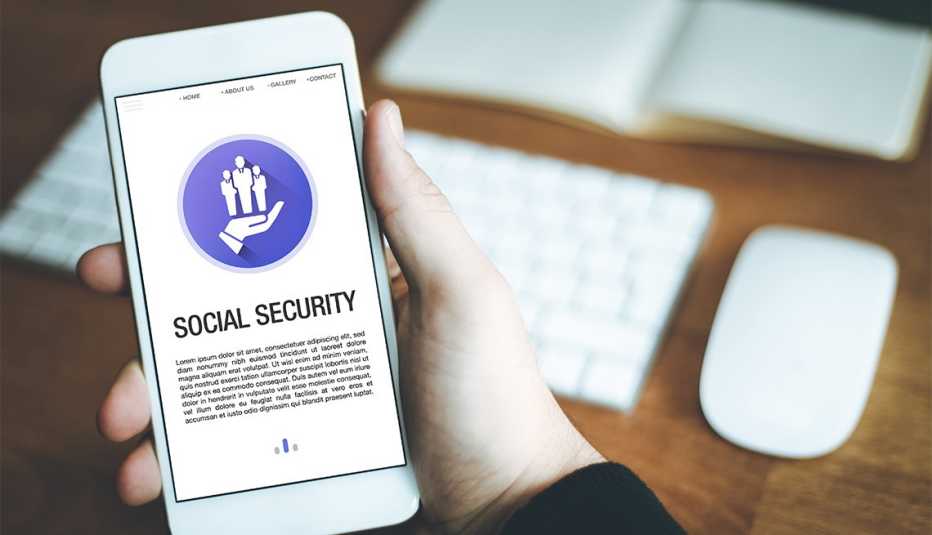 Social Security words displayed on a smartphone held in one hand over desk