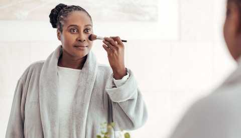 A woman applies foundation on her face with a brush