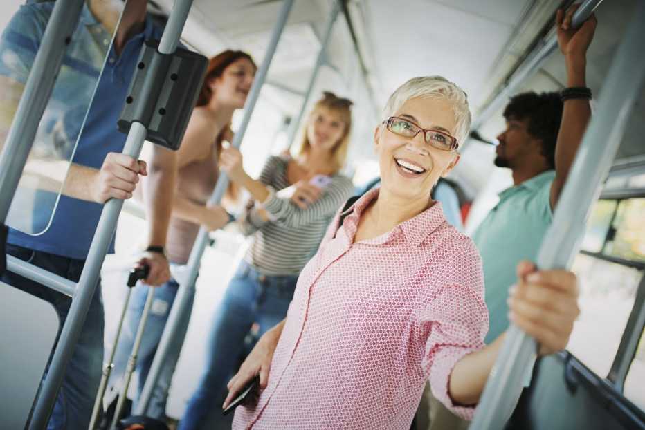 Older Caucasian woman riding public transportation with a blurred background of other riders behind her