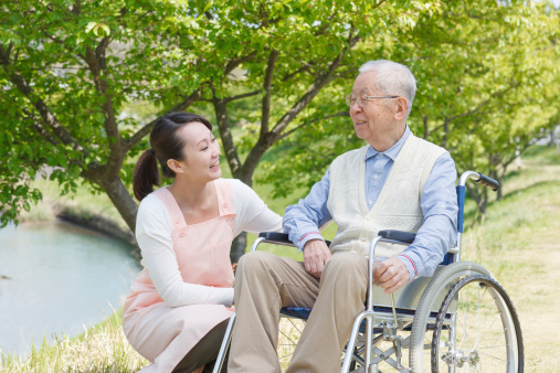 Senior man sitting on a wheelchair with caregiver
