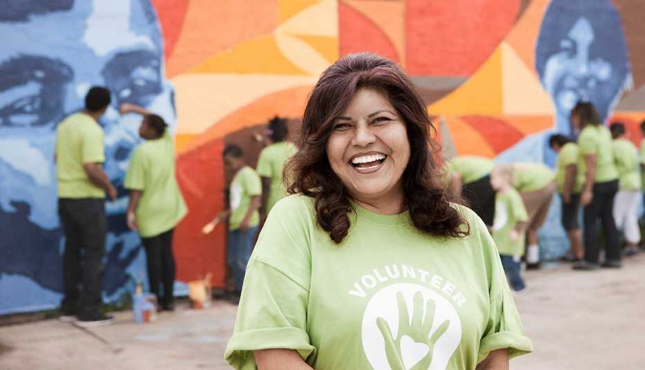 A woman smiles while a group of community volunteers paint a wall behind her.