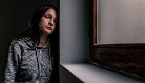 young woman looking depressed, staring out of a window