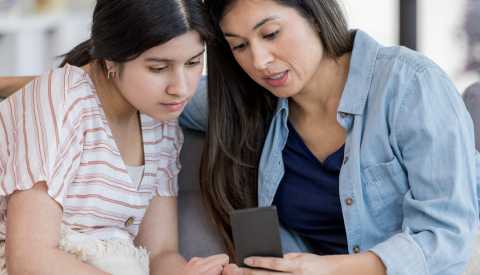 mother and her teenage daughter looking at phone together