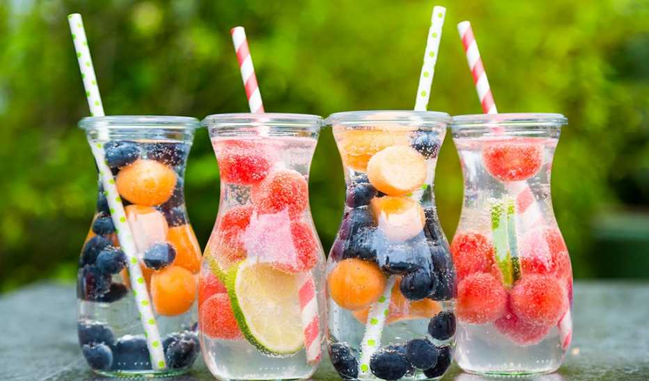 Four carafes of fruit-infused water on a table outside
