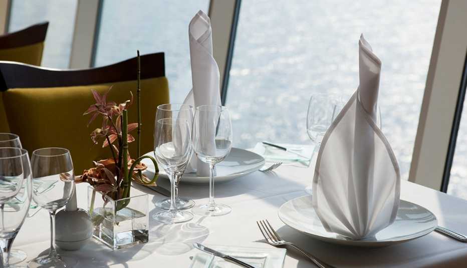 Table set with plates, glasses, napkins and silverware next to window overlooking a body of water table set with plates, glasses, napkins and silverware next to window overlooking a body of water