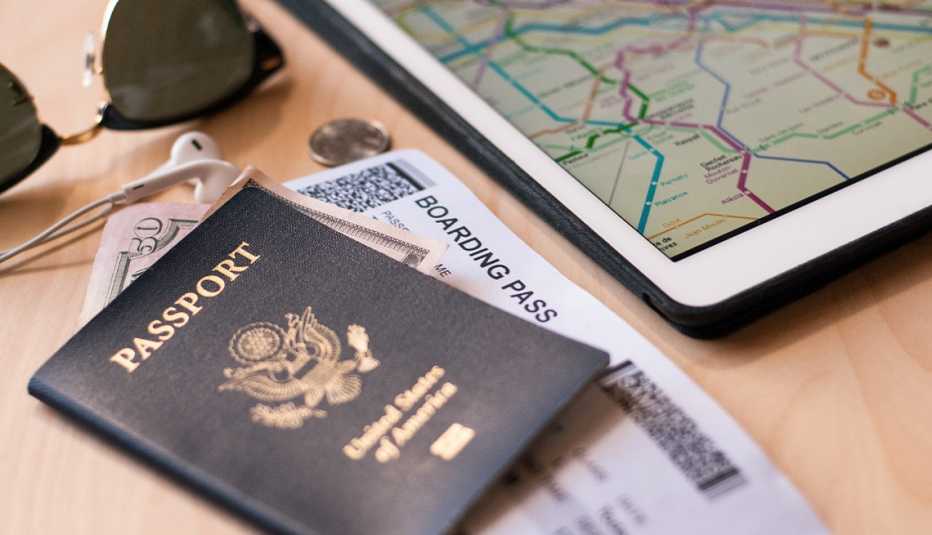 Passport with boarding pass and 50 dollar bill in it; headphones, sunglasses and ipad on table passport with boarding pass and 50 dollar bill in it; headphones, sunglasses and ipad on table