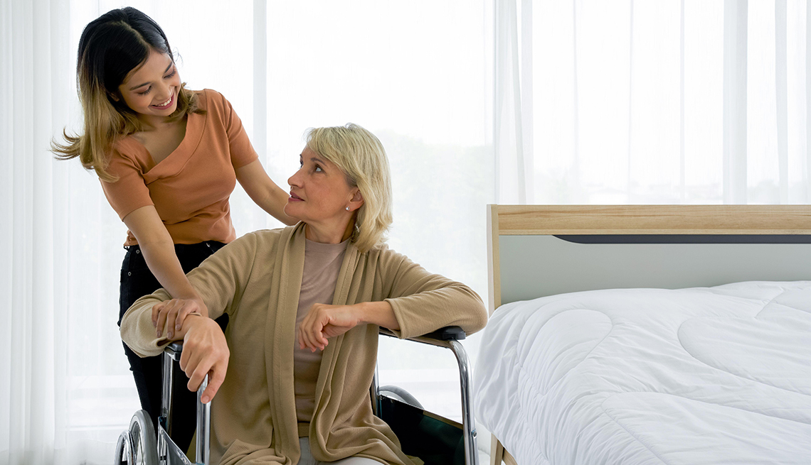 A girl standing next to her grandmother in a wheelchair in a hotel room