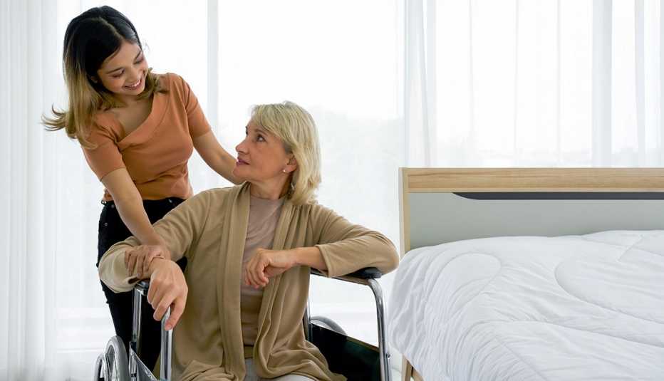A girl standing next to her grandmother in a wheelchair in a hotel room