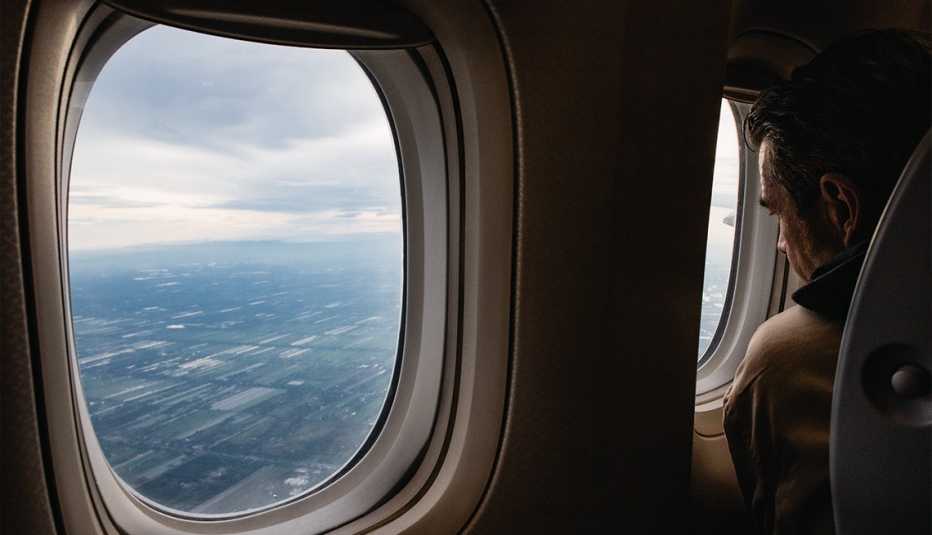 man looks out airplane window at clouds
