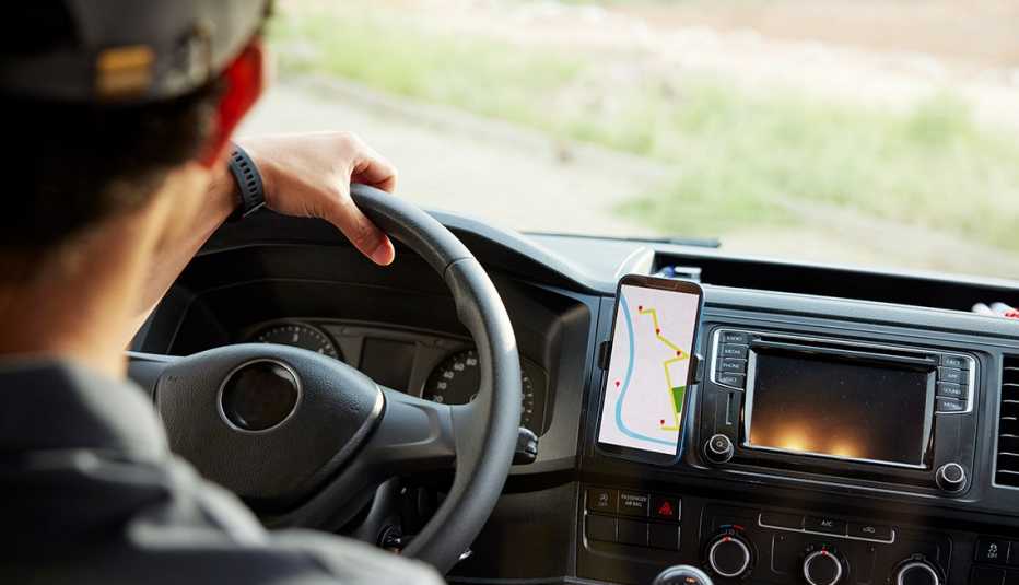back of man in car, holding onto steering wheel; phone with map on it to his right