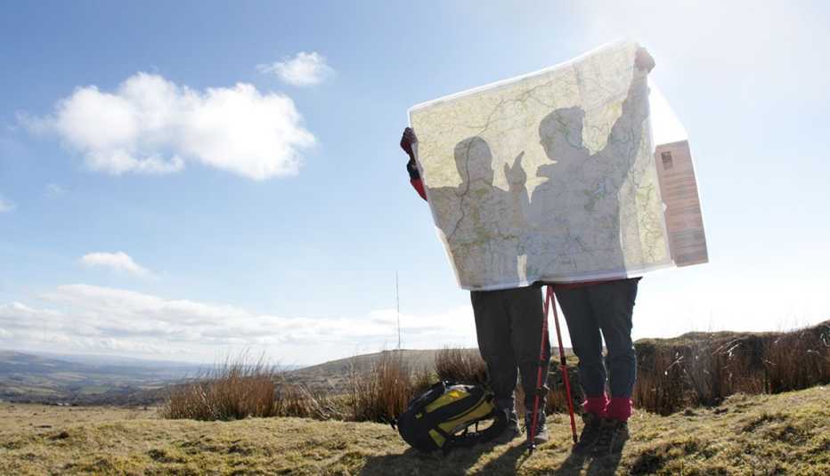 two hikers on a mountain in shadow behind a big map they're holding up 