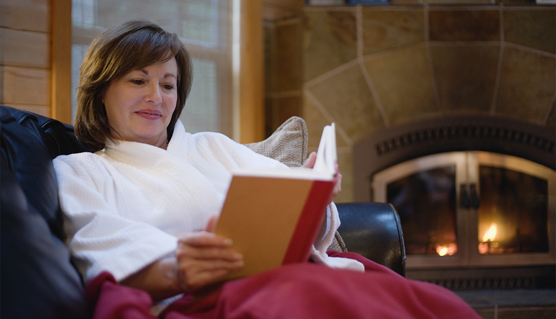 woman sitting on a couch, reading a book by the fire