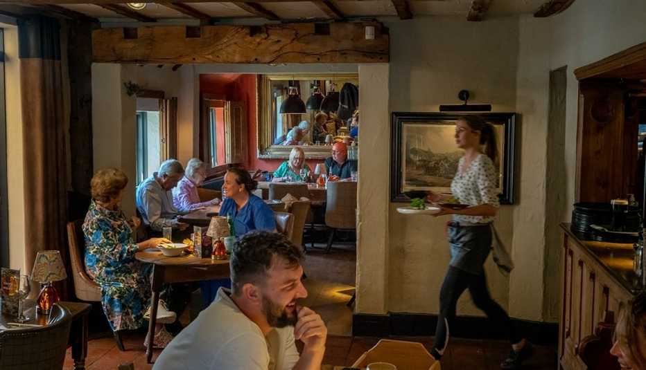 people sitting at tables inside restaurant; server carrying plates people sitting at tables inside restaurant; server carrying plates