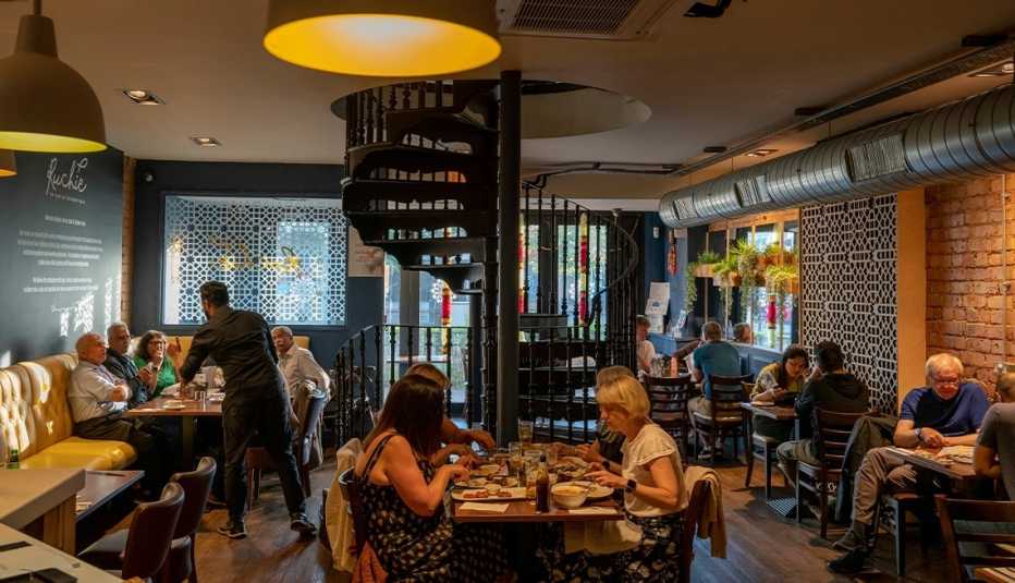 people sitting at tables inside restaurant; spiral staircase in middle leading up to another floor people sitting at tables inside restaurant; spiral staircase in middle leading up to another floor