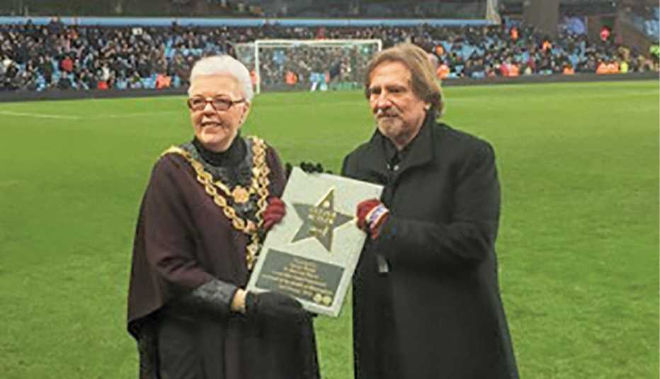 geezer butler receiving the walk of stars award from woman on the field at villa park; crowd in stands in the distance
geezer butler receiving the walk of stars award from woman on the field at villa park; crowd in stands in the distance