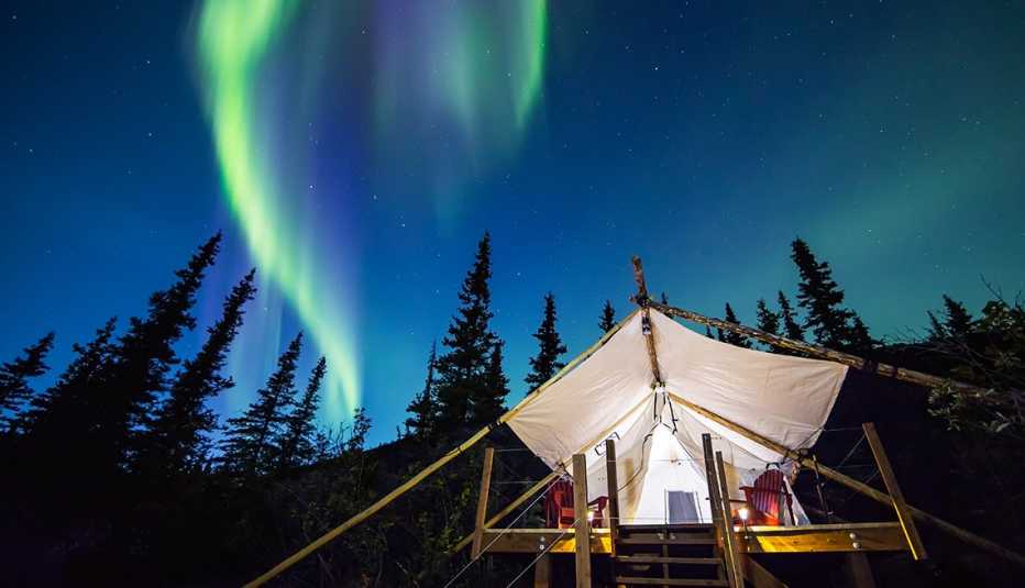 Aurora Borealis glowing green and pink over large canvas luxury camping tent in Alaska