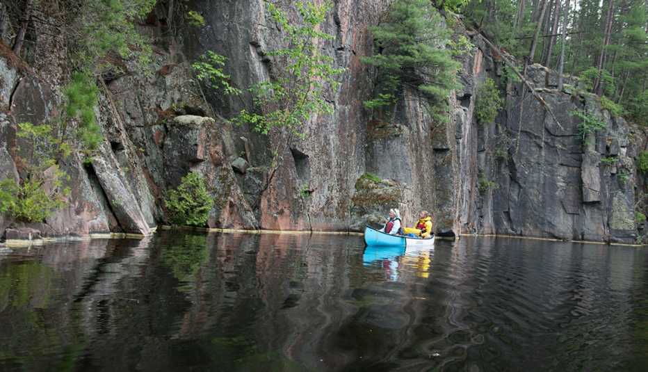 A photo of two people paddling a canoe in Quebec while looking at a rock face. A photo of two people paddling a canoe in Quebec while looking at a rock face.