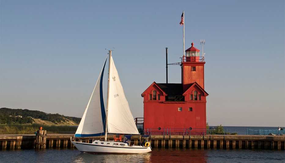 Sailboat entering harbor channel Holland State Park Michigan passing Big Red the entry lighthouse Sailboat entering harbor channel Holland State Park Michigan passing Big Red the entry lighthouse