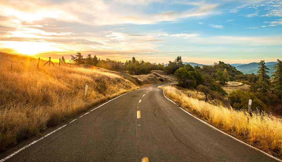 Curving two lane road through golden fields and deep green trees 