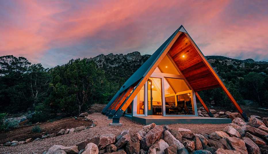 outside of small triangular shaped vacation home with glass doors; rocks in front of it, trees behind it