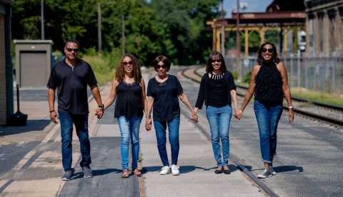 a family walks together along train tracks, smiling and holding hands