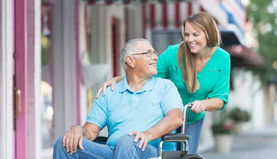 woman pushing a senior man sitting in a wheelchair on a sidewalk in front of stores