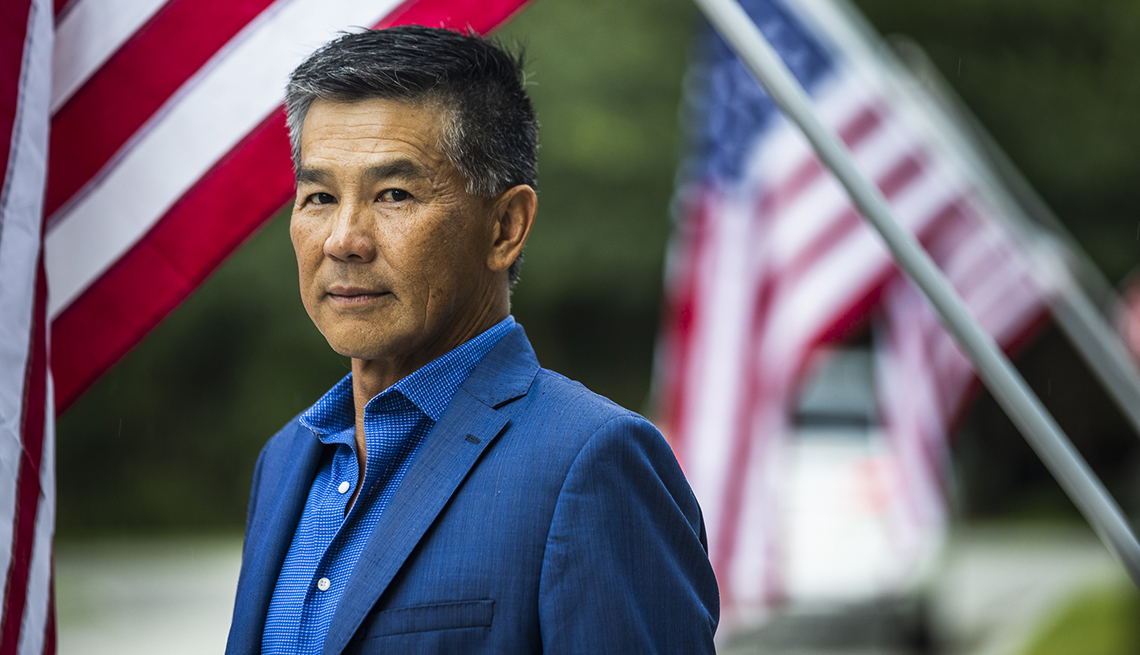 a man in a suit stands before american flags