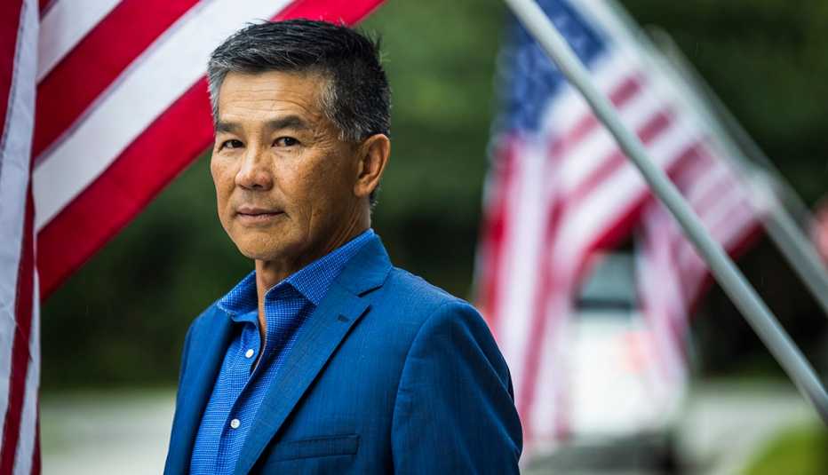 a man in a suit stands before american flags