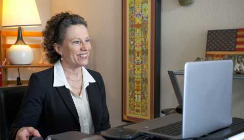 a woman sitting at her desk looking at a laptop a woman sitting at her desk looking at a laptop
