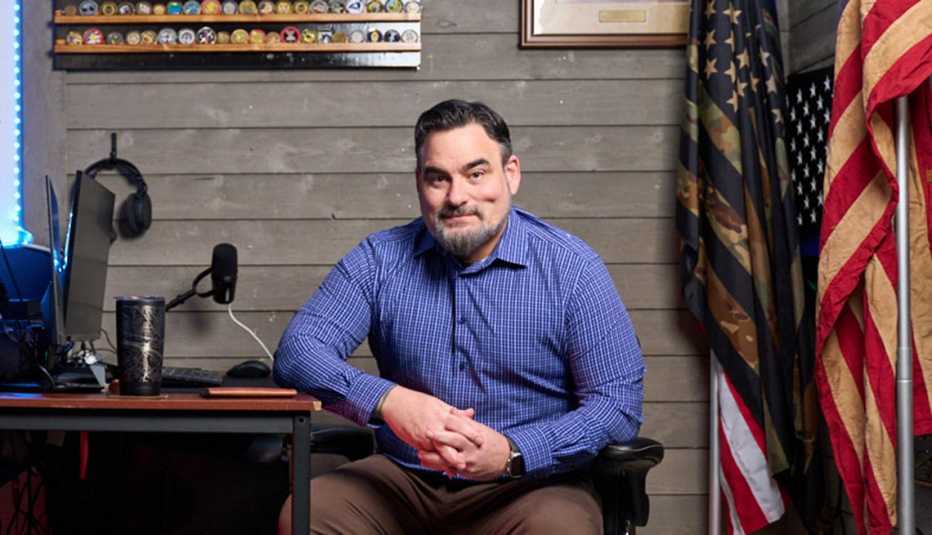 jason piccolo sits at a desk in front of a gray wall with an american flag.