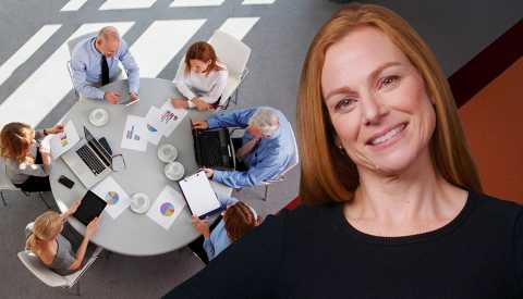 a woman smiling at the camera with workers at a table in the background