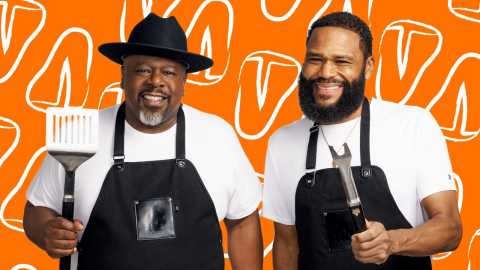 a photo shows Anthony Anderson and Cedric the Entertainer in front of a food-themed backdrop. They are wearing overalls and wielding grilling utensils