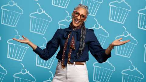 A photo shows Carla Hall in front of a dessert-themed backdrop