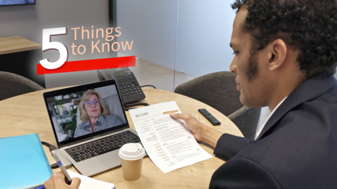 a man sitting at a table holding a resume talking on a video chat