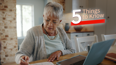 a woman sitting in front of a laptop  and taking notes with a pen and paper