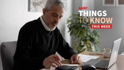 a photo shows a man sitting at a desk working with a calculator and a laptop