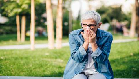 Woman sitting in the park and sneezing