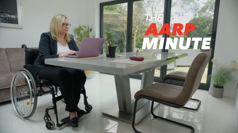 a woman in a wheelchair sitting at a desk using a laptop computer. A A R P minute