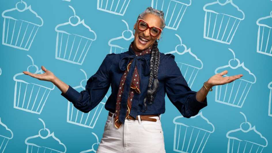 A photo shows Carla Hall in front of a dessert-themed backdrop